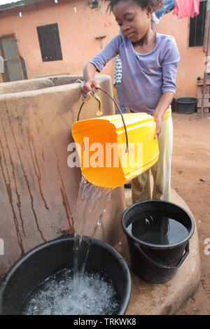Fillette togolaise versant de l'eau tirée d'un puits dans un seau. Lomé. Togo. Afrique de l'Ouest. Stock Photo