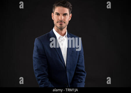 A good looking white male model modeling in a business suit, a half portrait, dark black background. He looks serious and confident. Stock Photo