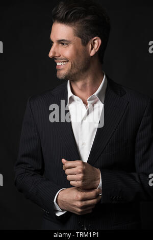 A good looking white male model modeling in a business suit, a half portrait, dark black background. He is smiling and looking away to the side. Stock Photo