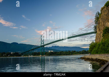 View of Lions Gate bridge from the seawall at the foot of steep cliff in Stanley Park, Vancouver, Canada. Stock Photo