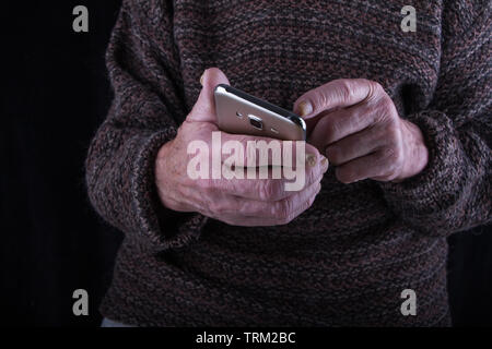Close up of a very old man's sore hands working with a smartphone against a dark background, selective focus, copyspace Stock Photo