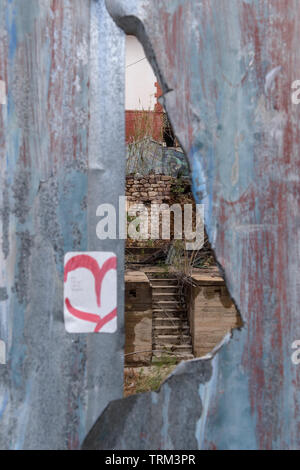 Bisbee, AZ/USA - 03-13-2019:  Opening in a metal fence exposes old building, Bisbee, AZ Stock Photo