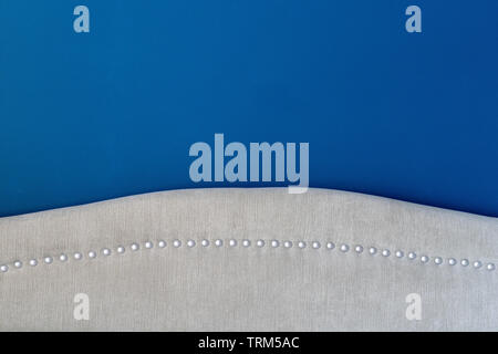 Deep royal blue painted wall with an upholstered headboard close up, showing the silver nail heads and beige fabric detail. Matching interior decor. Stock Photo