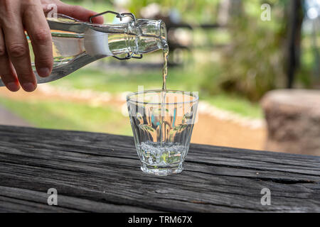 A waiter in a restaurant pours fresh water from a bottle into a glass, close up, outdoors Stock Photo