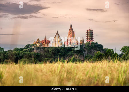 Cottage on paddy rice field with Buddhism church on hill at Wat Tham Sua, Tiger Cave, Kanchanaburi, Thailand Stock Photo