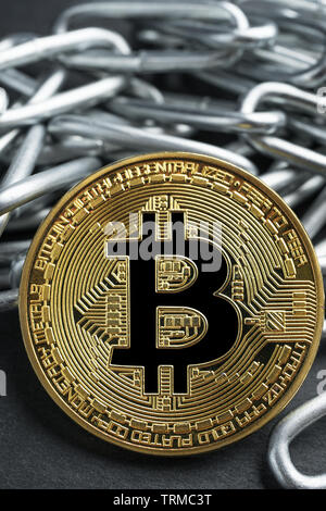 Physical Bitcoin gold coin on a convoluted shiny metal chain on dark stone slate plate background. Cryptocurrency legal restrictions abstract concept. Stock Photo
