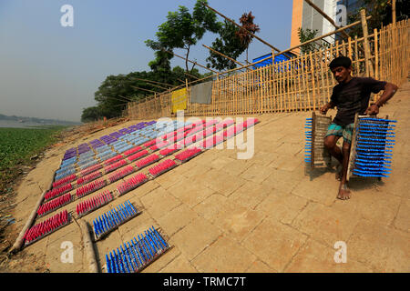 A laborer dries racks of rubber balloon in the sun as he works at a balloon factory in Dhaka, Bangladesh. Stock Photo
