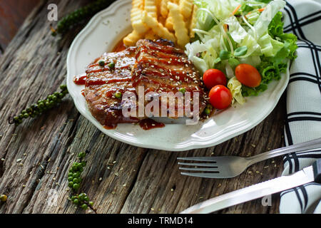 Pork steak with sauce in a white plate on a wooden table Stock Photo