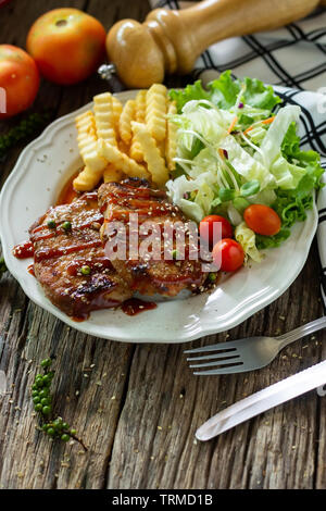 Pork steak with sauce in a white plate on a wooden table Stock Photo