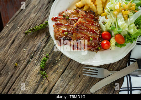 Pork steak with sauce in a white plate on a wooden table Stock Photo