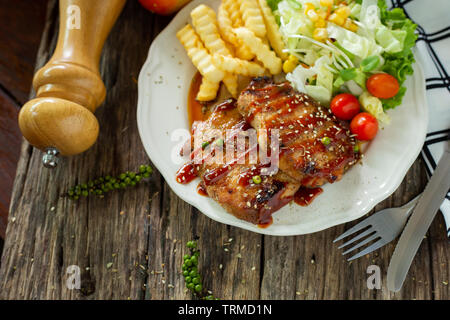 Pork steak with sauce in a white plate on a wooden table Stock Photo