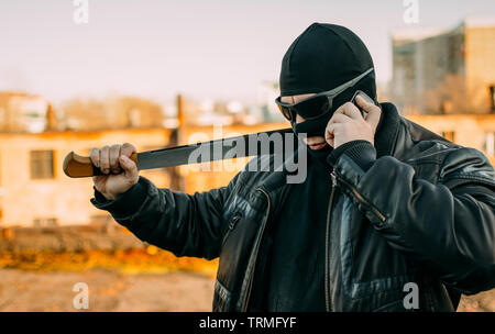 bandit with a machete in a black mask talking on the phone Stock Photo