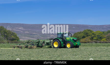 Contractor rowing up grass for silage with a Krone Swadro rake pulled by a John Deere 6145R, Lancaster, Lancashire, UK. Stock Photo