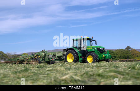 Contractor rowing up grass for silage with a Krone Swadro rake pulled by a John Deere 6145R, Lancaster, Lancashire, UK. Stock Photo