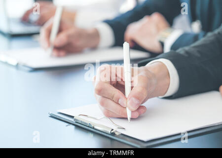 Business people sitting in a row and writing notes. Close-up of writing hands. Stock Photo