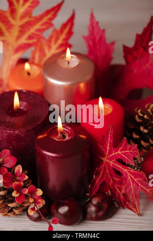 Autumn still life - candles, leaves and cones on the background of pillows. Selective focus. Stock Photo