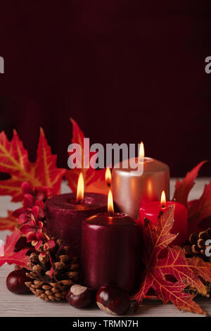 Autumn still life - candles, leaves and cones on the background of pillows. Selective focus. Stock Photo
