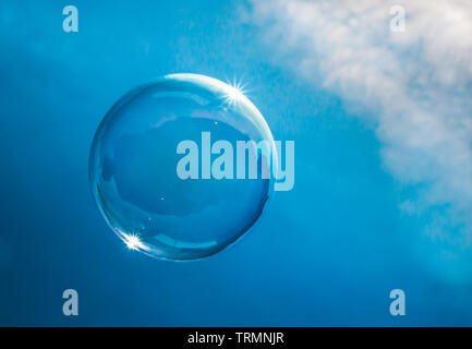 Soap bubble floating in a blue sky with clouds catching the sunlight on its edge. Fragile earth or blue planet concept Stock Photo