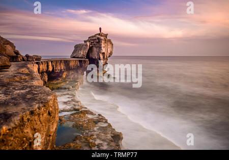 Man standing on top of Pulpit Rock at sunset, Portland Bill on the Isle of Portland near Weymouth on Dorset's Jurassic Coast. England. UK. Stock Photo