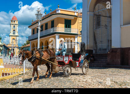 Horse carriage driving through Plaza Mayor looking for a fare with the bell tower of Church of St. Francis in the background Trinidad, Cuba,Caribbean Stock Photo