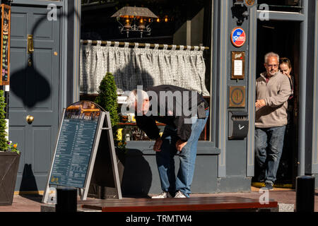 Man tourist reading restaurant outdoor menu board while bending his back in funny way. Stock Photo