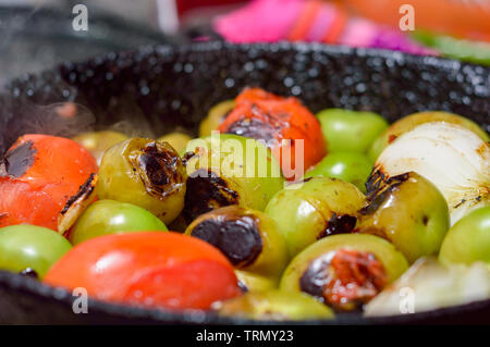 Cooking Mexican green sauce, salsa verde, made with tomatillos, tomatoes, onions, garlic chiles and cilantro. Sizzling pan and steaming vegetables, co Stock Photo