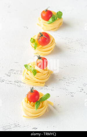 Raw fettuccine with cherry tomatoes and fresh basil leaves on the white background Stock Photo