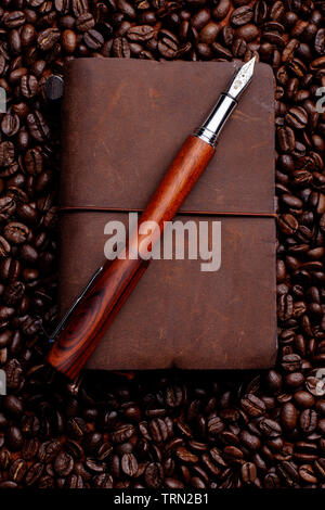 Open, posted Conklin Endura fountain pen with a small leather traveler's notebook on a background of coffee beans. Stock Photo
