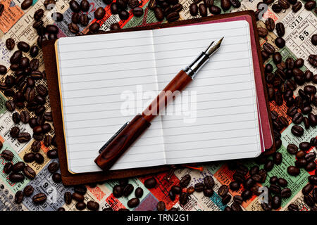 Opened Conklin Endura fountain pen resting on an opened small leather traveler's notebook on a background of tickets and scattered coffee beans. Stock Photo