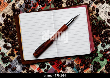 Opened Conklin Endura fountain pen resting on an opened small leather traveler's notebook on a background of tickets and scattered coffee beans. Stock Photo