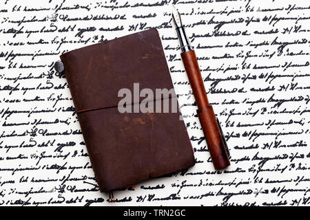 Opened Conklin Endura fountain pen with a small leather traveler's notebook on a background of cursive writing. Stock Photo