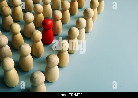 Unique red figurine stand out in the crowd from wooden ones. Stock Photo