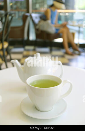 Vertical image of a cup of green tea and teapot on white table in a cafe Stock Photo