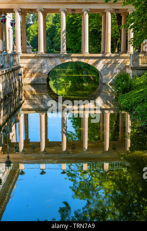 Lazienki Park in Warsaw, Poland, classical arch bridge with colonnade from 18th century over canal with water reflection, columned gallery in old Roya Stock Photo