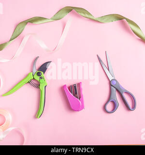 Florist tools for creating bouquets and caring for flowers - pruner and stapler with flowers on a pink table Stock Photo