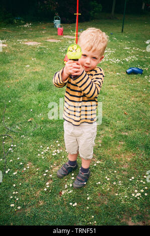 Two year old boy playing outside with a toy bubble gun, Medstead, Alton, Hampshire, England, United Kingdom. Stock Photo