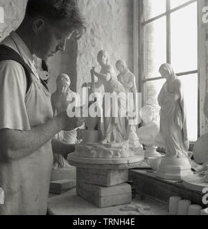 1950s, historical, a male craftsman standing by a window in a pottery or ceramic's studio, working on female figurines or statuettes, England, UK. Stock Photo