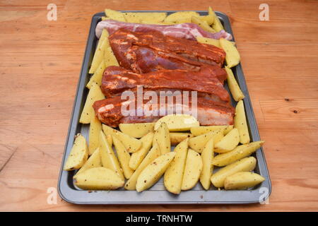 Juicy seasoned ribs with organic uncooked potato wedges on a silver flat baking tray Stock Photo