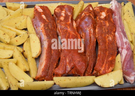 Juicy seasoned ribs with organic uncooked potato wedges on a silver flat baking tray Stock Photo