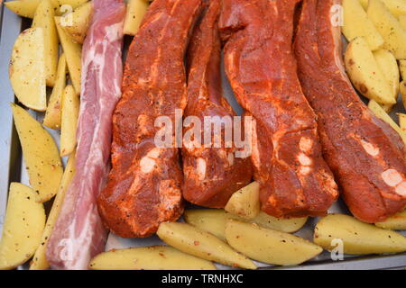 Juicy seasoned ribs with organic uncooked potato wedges on a silver flat baking tray Stock Photo