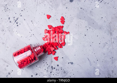 Transparent bottle with red sugar hearts to decorate baking and cakes on a gray table. Valentine's day concept. Top view, flat lay, Stock Photo