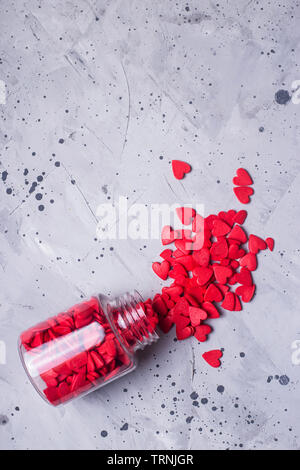 Transparent bottle with red sugar hearts to decorate baking and cakes on a gray table. Valentine's day concept. Top view, flat lay, Stock Photo