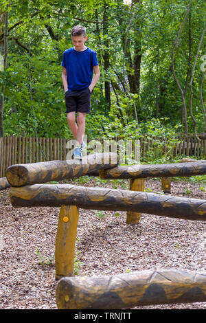 Young 11 year old caucasian boy outdoors in summer playing balancing on wooden snake at natural playground a play area constructed of sculpted wood Stock Photo