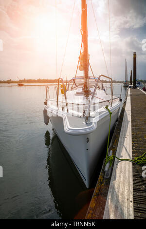 Sailing yacht moored on a wooden pontoon in a tranquil harbour as the sun sets, viewed from the bow. Stock Photo