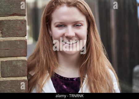Portrait Of Smiling Teenage Girl Leaning Against Wall In Urban Setting Stock Photo
