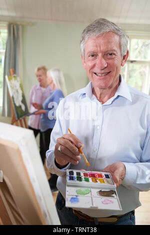 Portrait Of Senior Man Attending Painting Class With Teacher          In Background Stock Photo