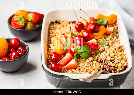 Fruits and berries oat crumble in oven dish on a gray background. Stock Photo