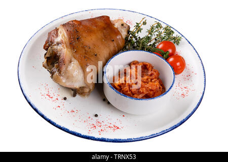 Pork knuckle with tomatoes and sauerkraut on a round light plate with a blue border, on a white isolated background, a view at an angle. Stock Photo