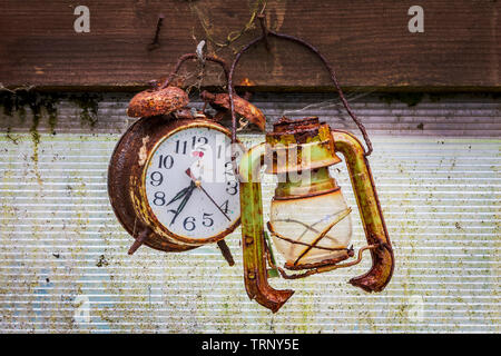 Old and rusty alarm clock hanging on a nail next to an old broken lantern, in a garden shed Stock Photo