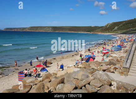 People enjoying a sunny summers day on the beach in Sennen Cove, Cornwall, England, UK showing the sandy beach and blue sea under a blue sky. Stock Photo